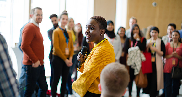 a woman with a microphone talking to people in a group around her